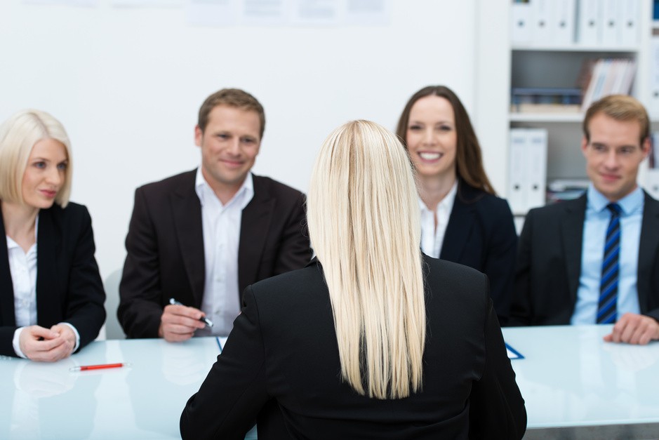Young female job applicant in an interview sitting with her back to the camera facing a row of personnel executives